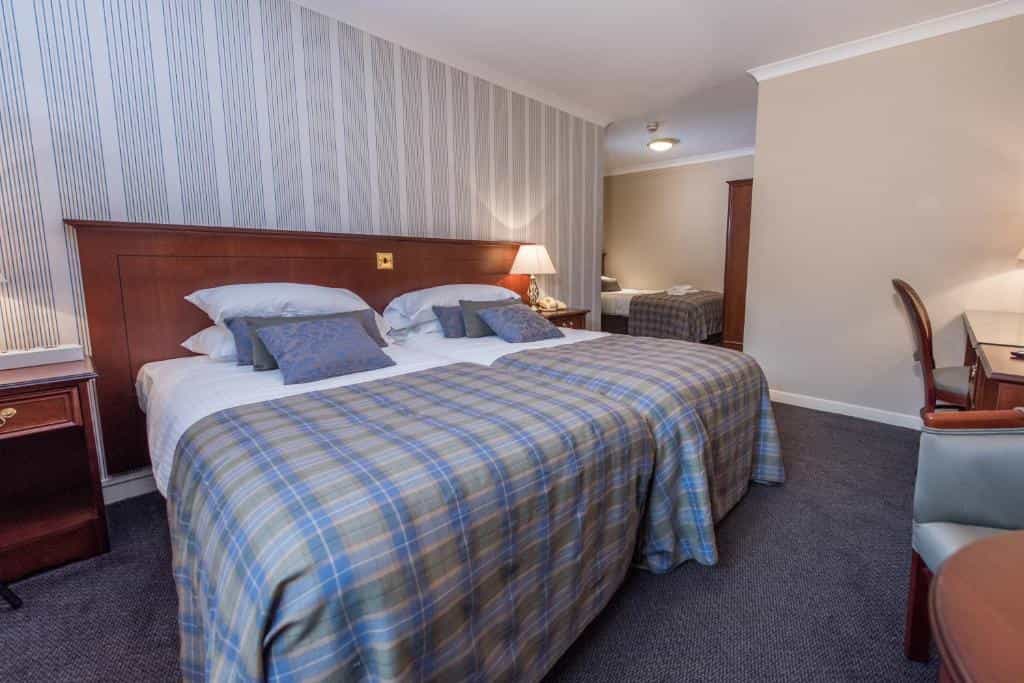 Twin beds with blue plaid blankets in a hotel room, view into an adjoining room.
