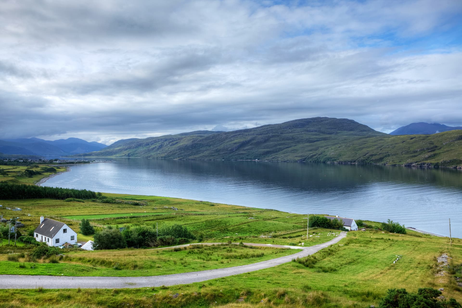 Lochside view in Ullapool with green hills, white cottages, and dramatic cloudy sky.