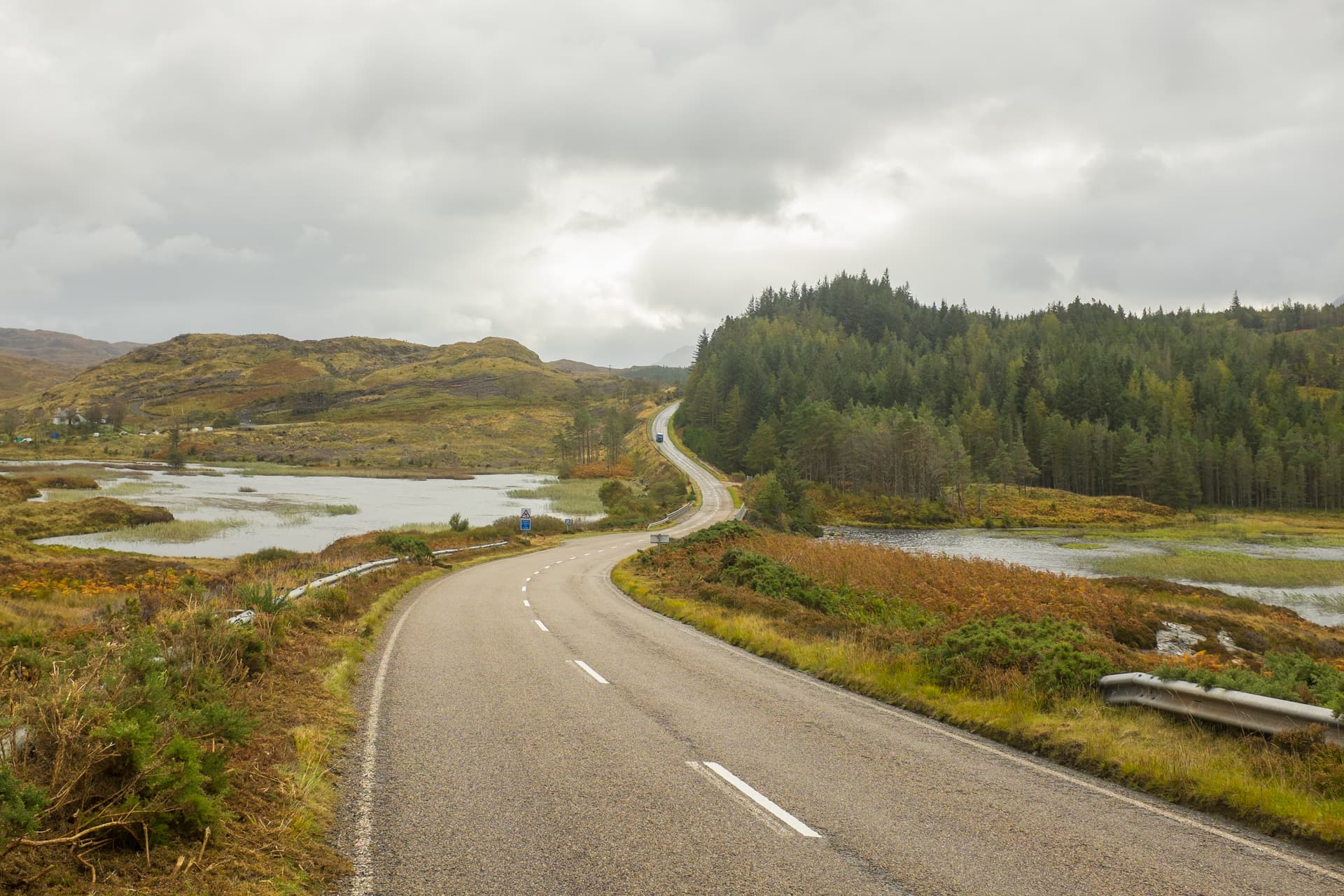 Winding road near water and hills with autumn foliage under a cloudy sky near Scourie.