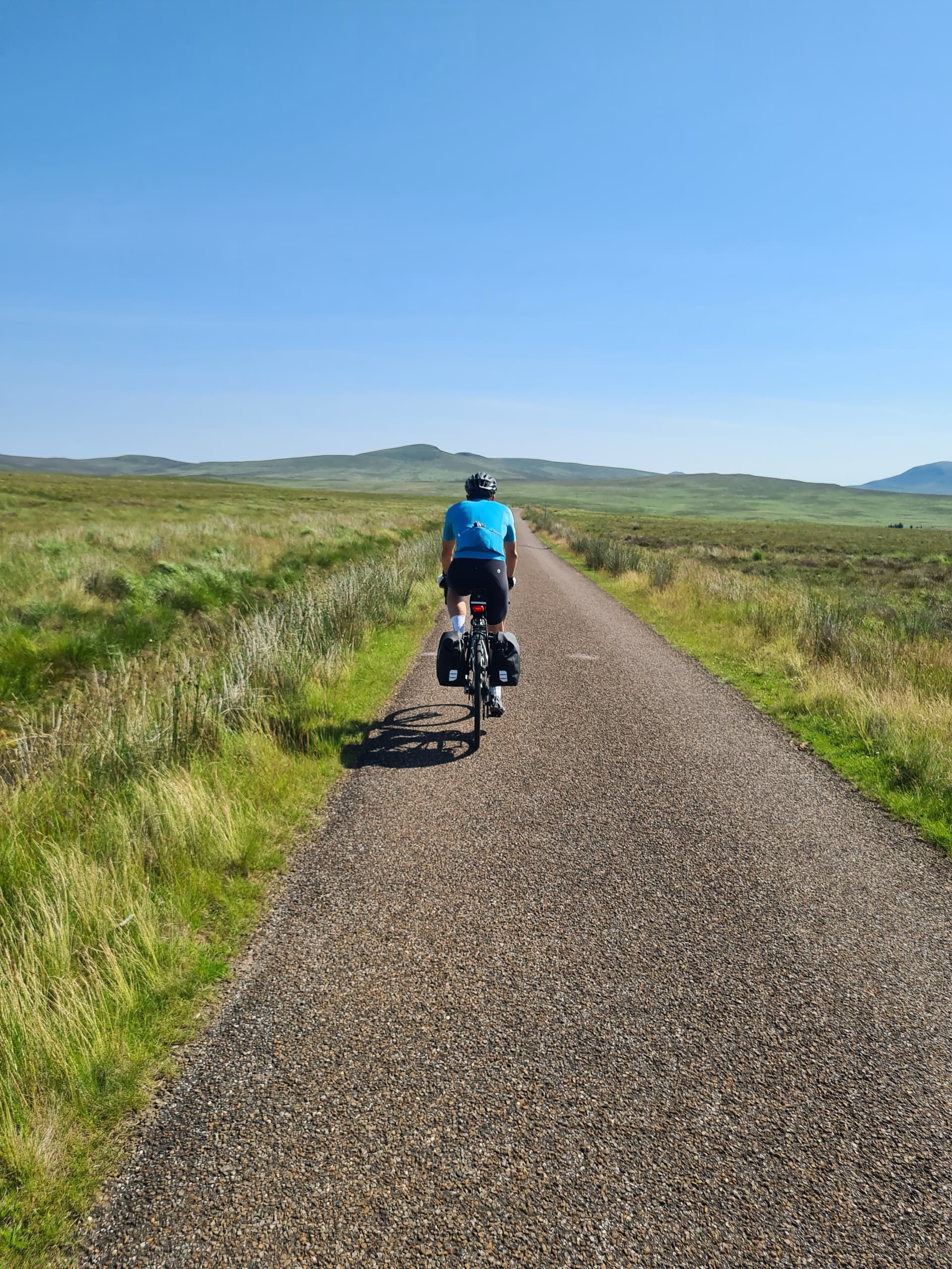 Cyclist riding touring bicycle on paved single track through moorland landscape