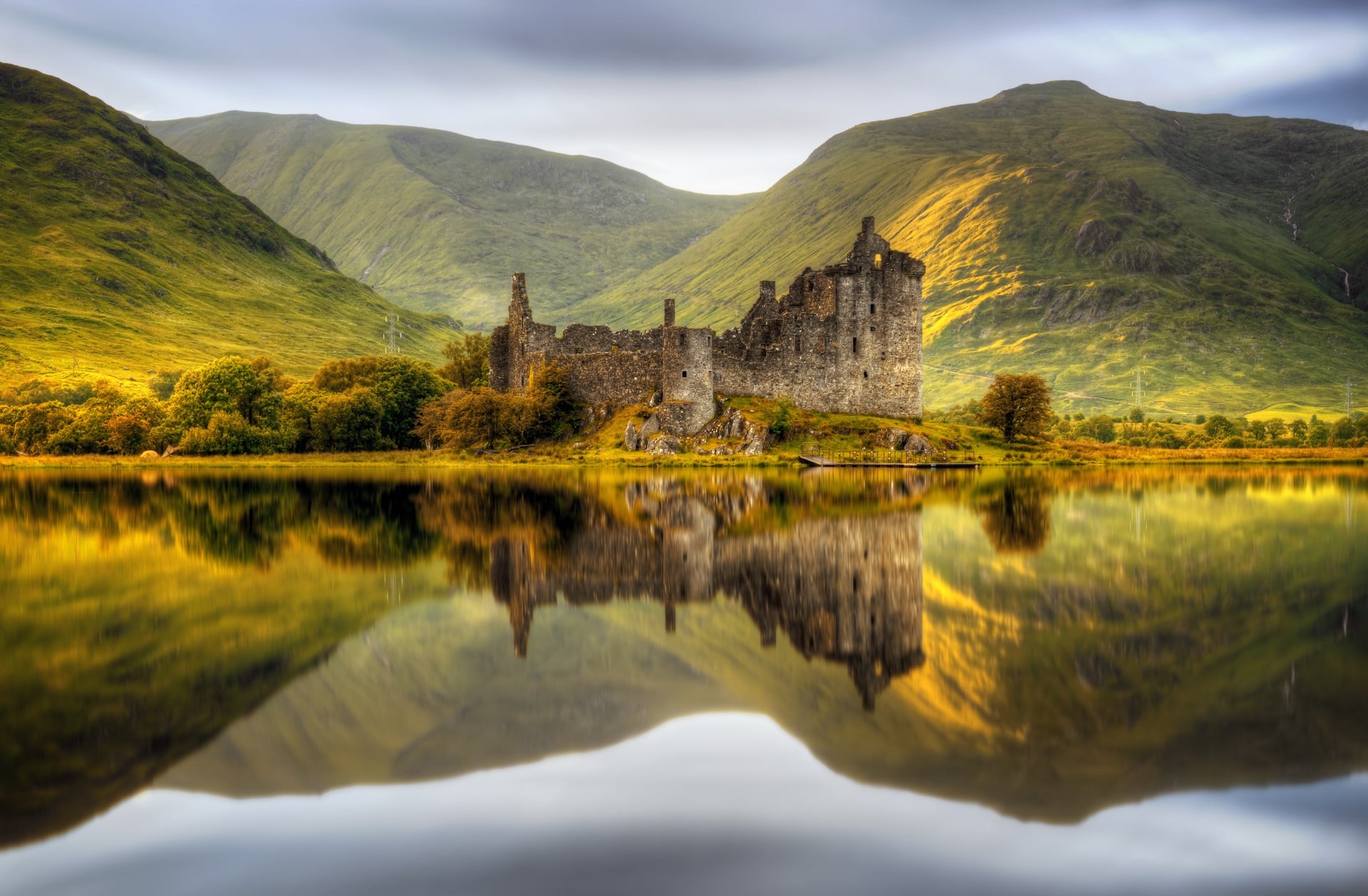 Kilchurn Castle ruins reflected in water with green mountains at sunset