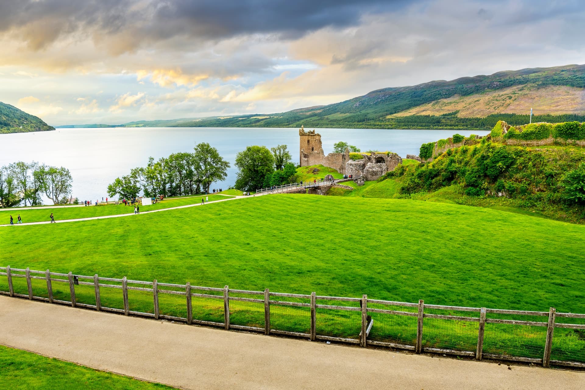 Urquhart Castle ruins beside Loch Ness with green lawn and dramatic cloudy sky