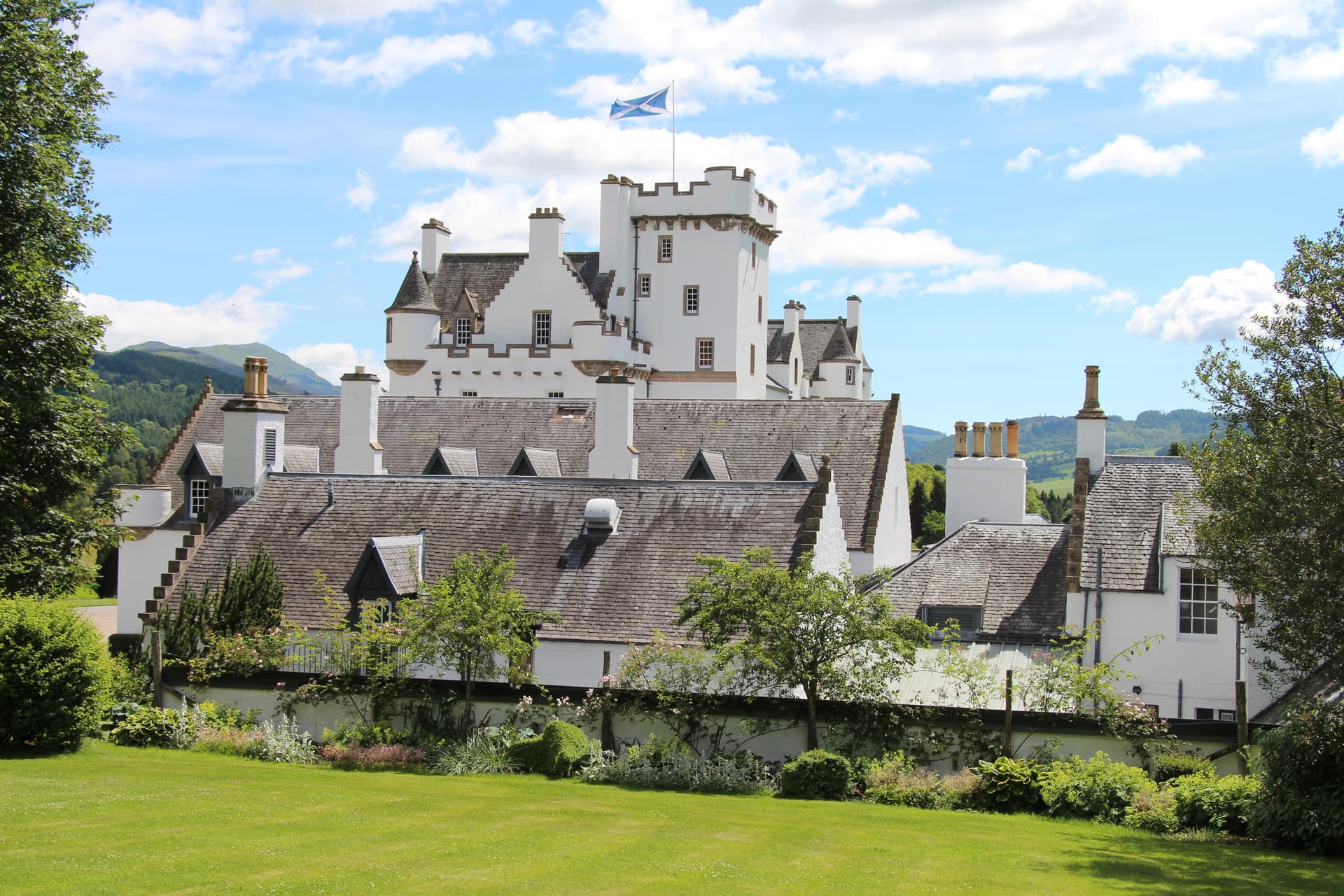 White castle with Scottish flag flying, set against green hills under a blue sky.