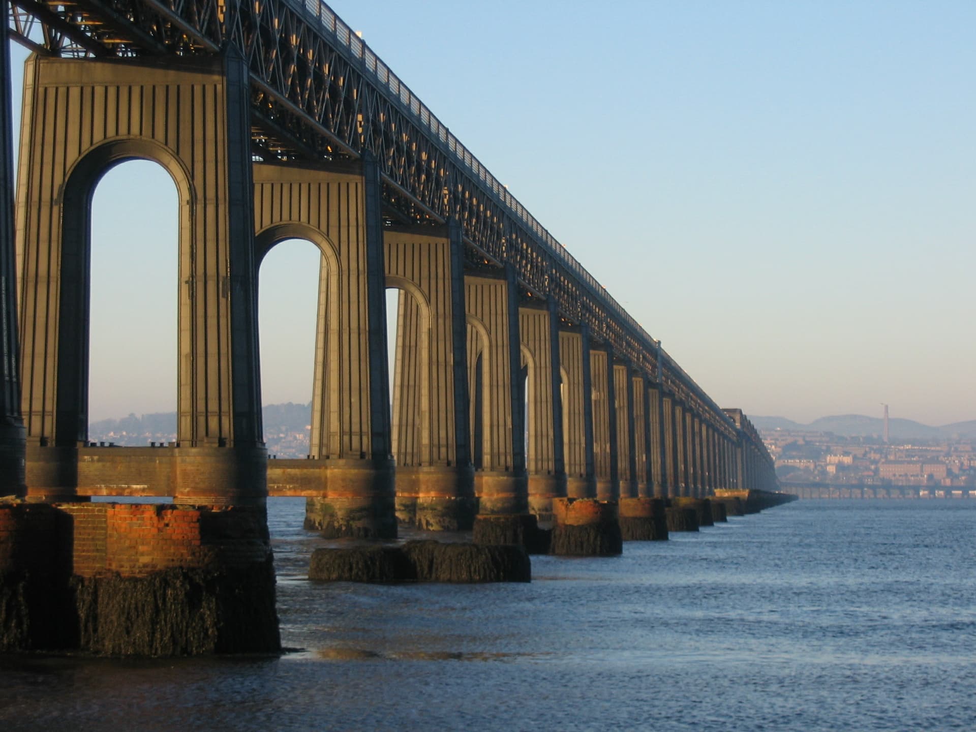 Massive railway bridge piers extending over water toward a distant city skyline.