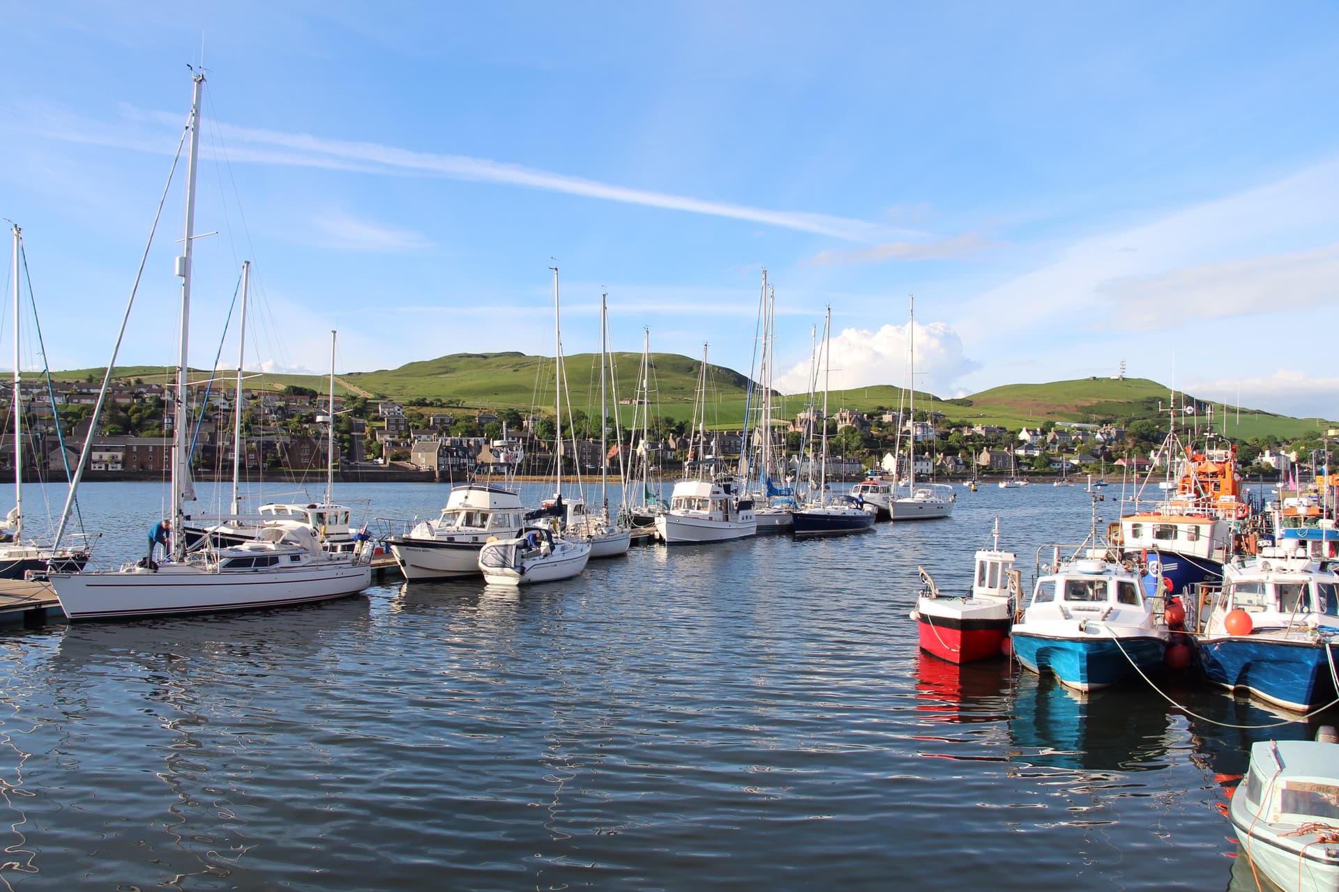 Sailboats and fishing boats docked in Campbeltown harbor with green hills in the background.