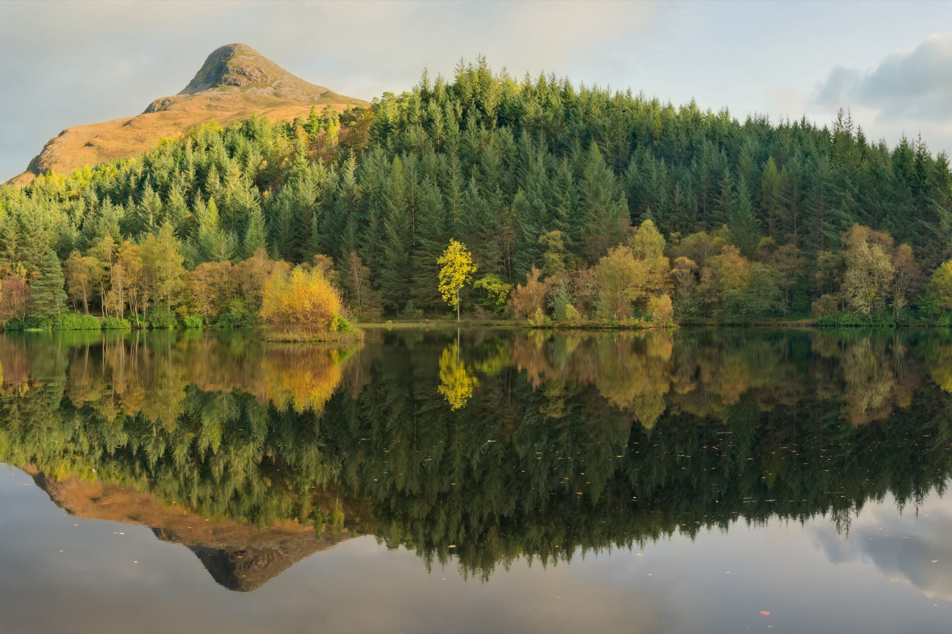 Scottish Highlands lake reflecting pine forest and mountain with autumn foliage